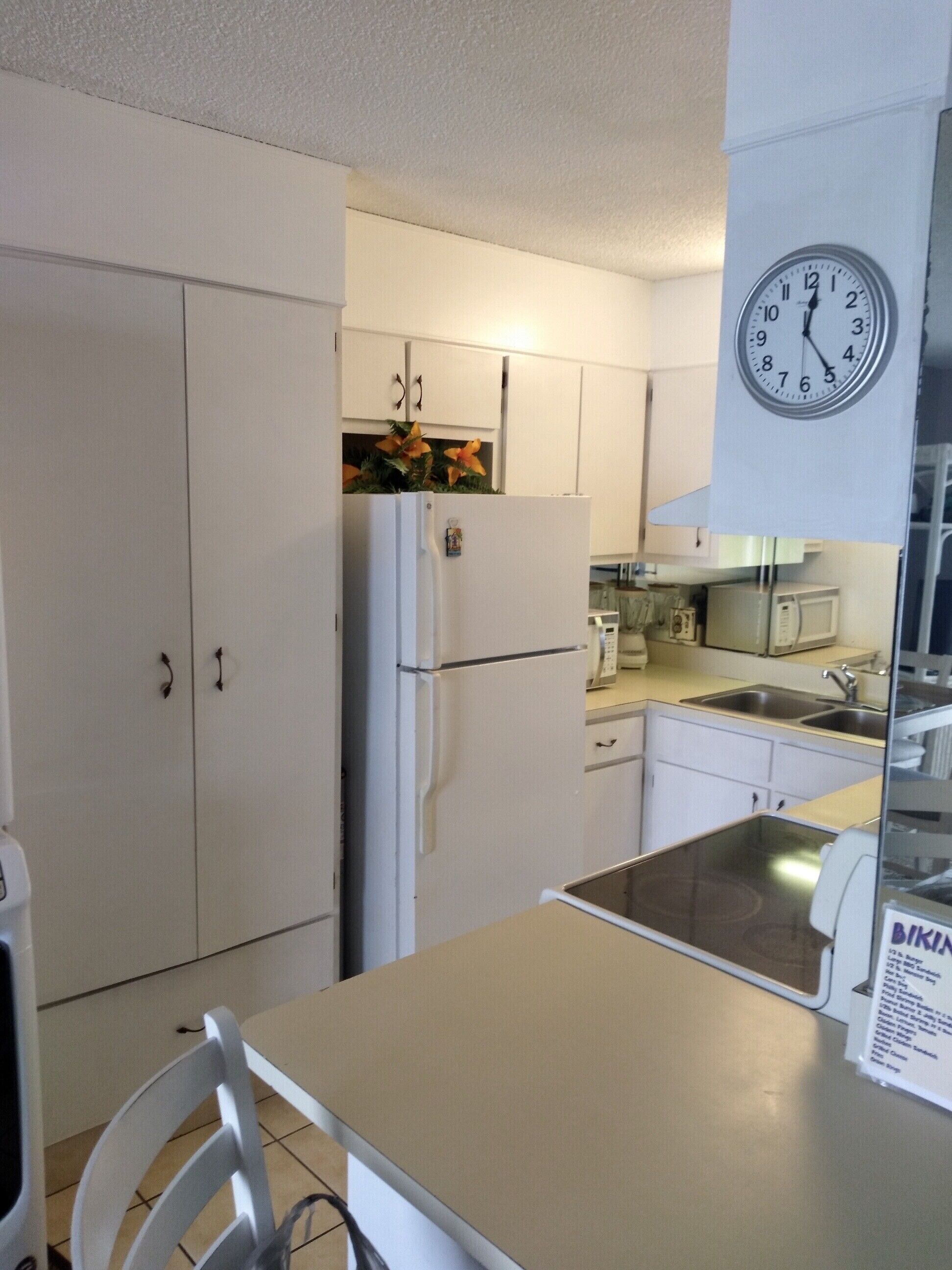 A compact kitchen with white cabinets, a refrigerator, a microwave, and a clock.