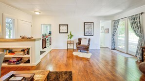 Un salón amplio con pisos de madera, un sillón de cuero marrón, una estantería y un ventanal con cortinas.
