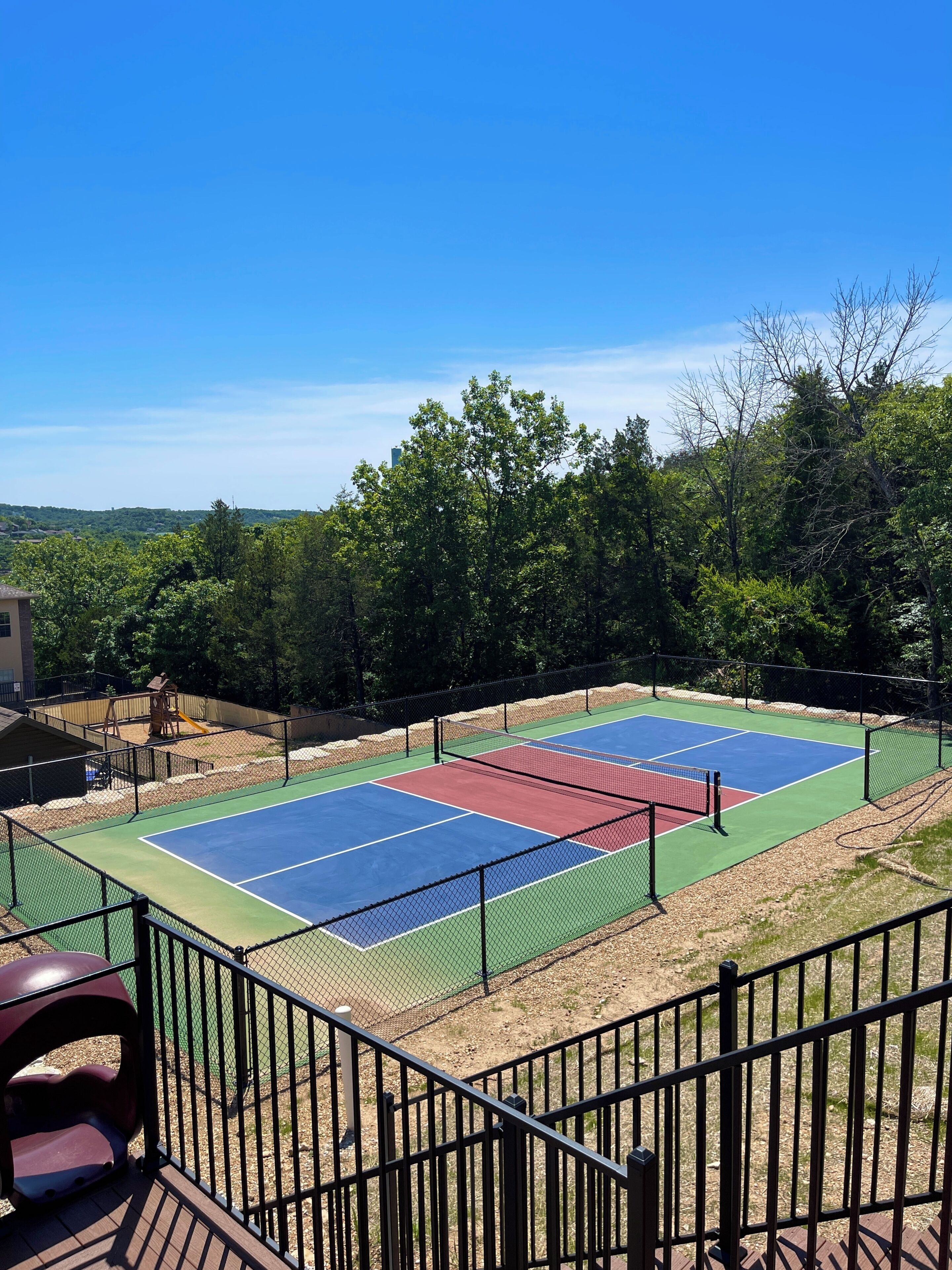 A tennis court with a net, surrounded by a fence, and trees in the background.