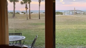 Eine Terrasse mit Tisch und Stühlen, mit Blick auf eine Rasenfläche mit Palmen und eine Holzbrücke zum Strand.