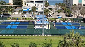 A tennis court with multiple courts, surrounded by greenery and buildings.