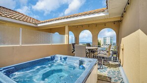 A rooftop terrace with a hot tub, outdoor seating, and a view of the ocean and buildings.