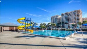 A swimming pool with a yellow water slide, surrounded by palm trees and hotel buildings.