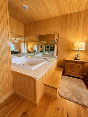 Un bagno con rivestimenti in legno, una vasca da bagno ampia, uno specchio e un mobile bagno in legno con cassetti.