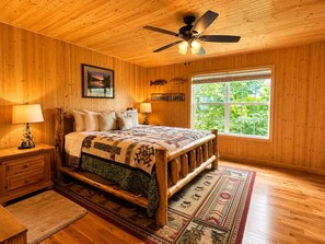 Ein Schlafzimmer in einer Holzhütte mit einem Bett, Nachttischen, einem Deckenventilator, einem Fenster mit Blick und einem Schild mit der Aufschrift 'FISHERMAN'S LODGE'.