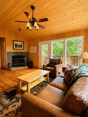 A cozy living room with a fireplace, wooden ceiling, and large windows.