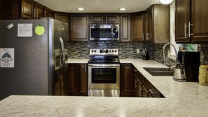 A kitchen with dark wooden cabinets, stainless steel appliances, a tiled backsplash, and a marble countertop. - Y-Knott Lodge! Relax on the shores of Toledo Bend! (Many)