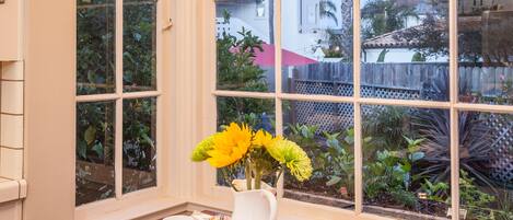 Un comedor con una mesa dispuesta para dos personas, un florero con flores amarillas y vistas al exterior a través de amplios ventanales.