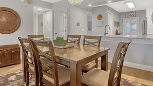 Un comedor con una mesa y sillas de madera, una araña y una cocina al fondo.