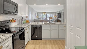 Una cocina moderna con armarios blancos, microondas integrado, lavavajillas y encimera de granito.