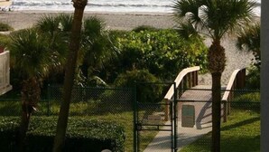 Vista de una playa con palmeras y un área cercada con un sendero que lleva a un edificio.