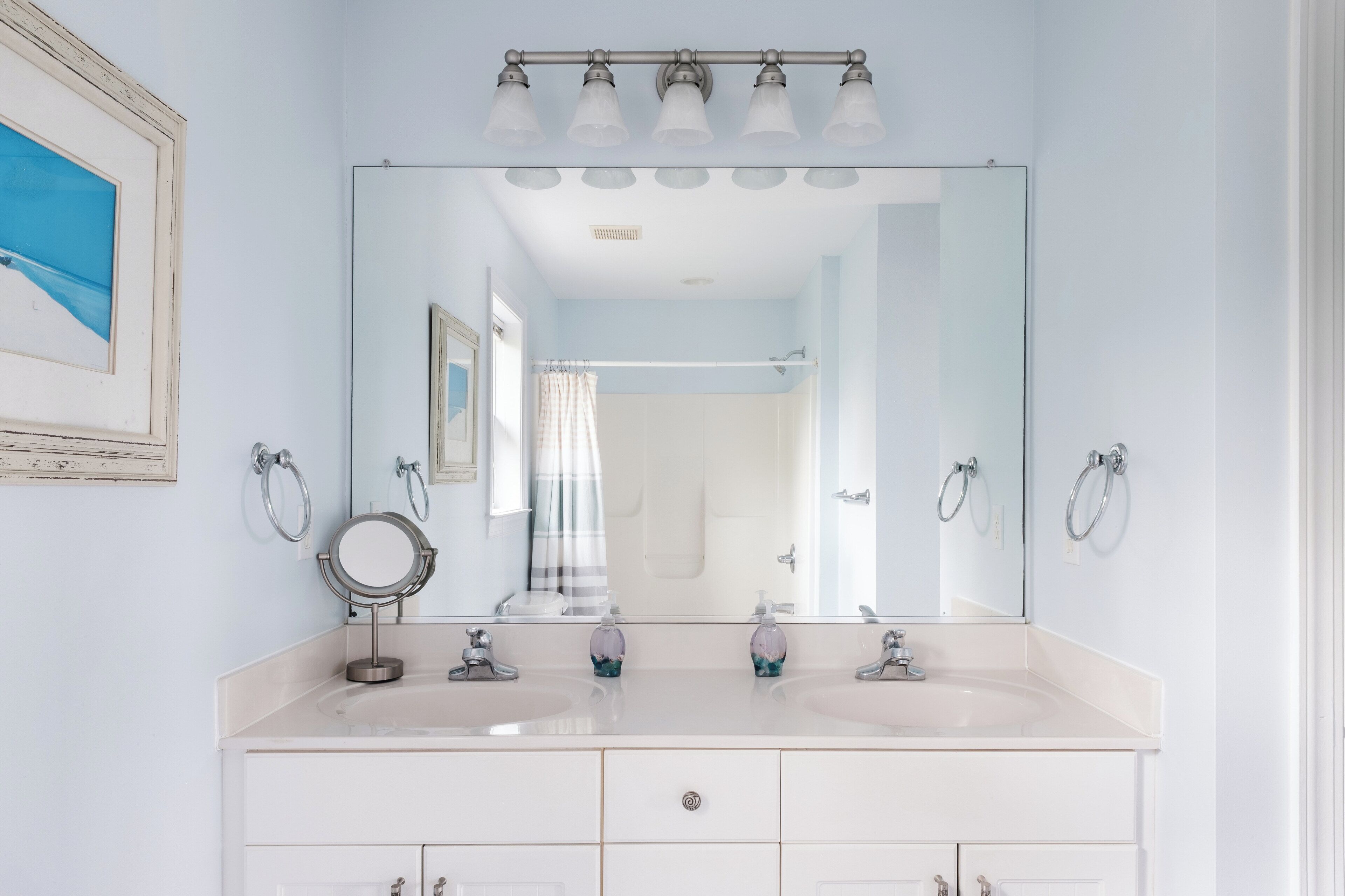 A bathroom with a large mirror, two sinks, a vanity with drawers, a towel ring, and a shower curtain.