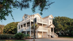 A two-story house with a balcony, a front porch, and a staircase leading to the entrance. - DolphinInnOBX Steps to beach 7BR Pool, Gym, Pickleball/Tennis, Pirate Ship, Golf (Southern Shores)