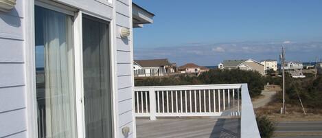 A residential building with a balcony, a view of the ocean, and neighboring houses.