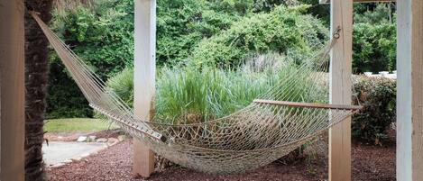 Una hamaca bajo una pérgola de madera en un jardín con follaje denso y cobertura de mantillo.