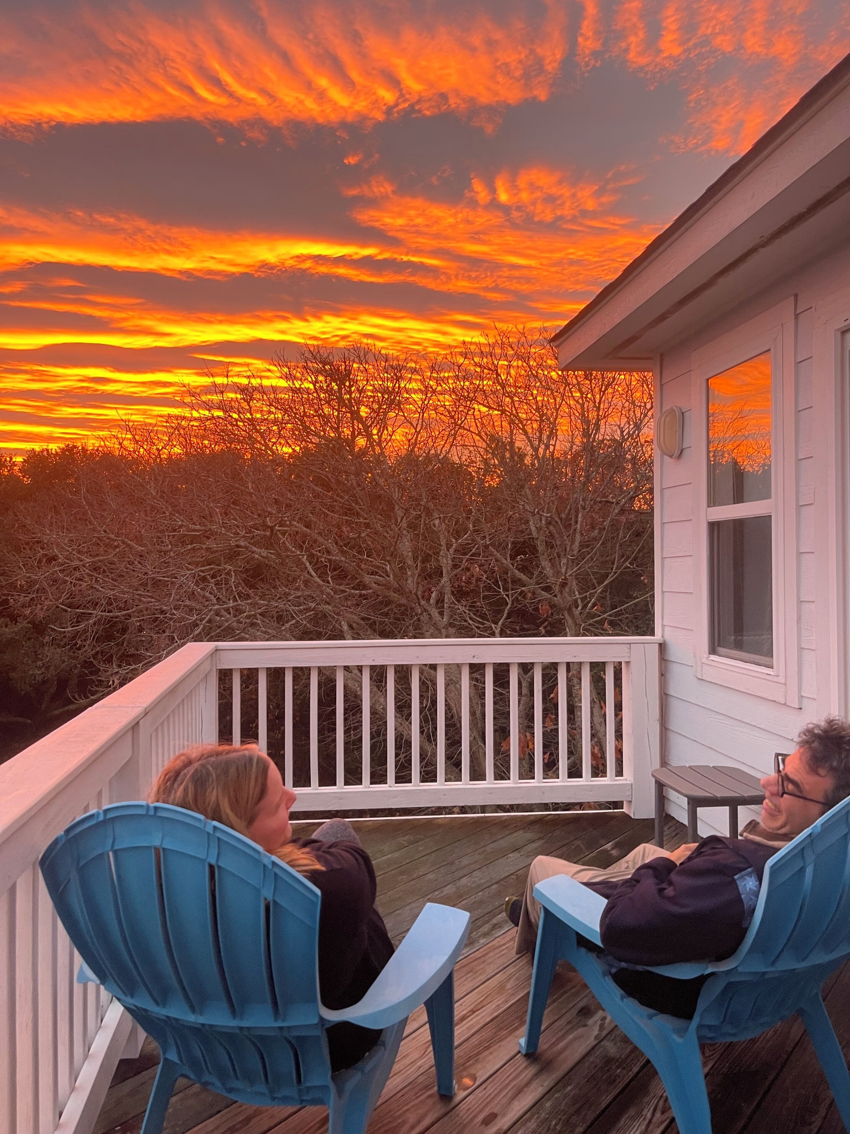A wooden deck with two chairs and a table, overlooking a house with a white railing and a window.