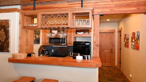 Una cocina con armarios de madera, microondas, cafetera y una estantería para vinos.