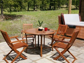 Une terrasse extérieure avec une table ronde en bois et quatre chaises en bois. On y trouve une petite plante en pot, une tasse rouge et un plateau noir.