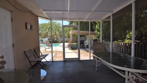 A covered patio with a glass door leading to a backyard, a glass table, and a chair. - Private Large Pool Getaway Near Siesta Key Gulf Gate Home (Sarasota)