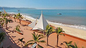 A beachside view with a sandy walkway lined with palm trees and white tents.
