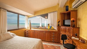 A hotel room with a bed, a desk with a TV, a chair, and a view of the beach.