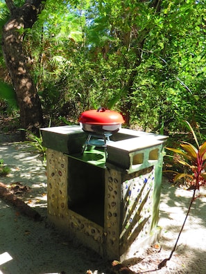 A portable barbecue grill with a red lid, placed on a concrete base with decorative elements.