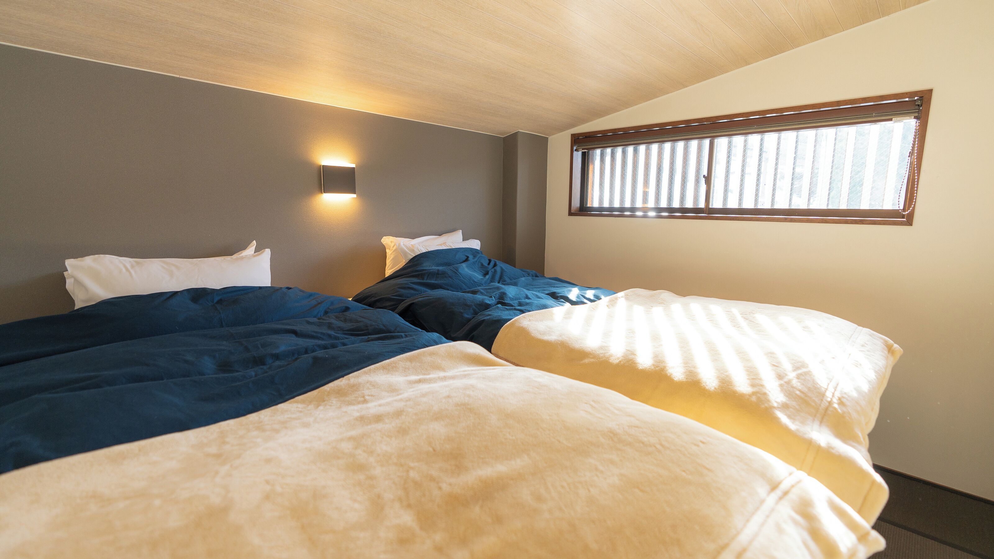 Habitación de hotel con dos camas, una lámpara de pared y una ventana con persianas.