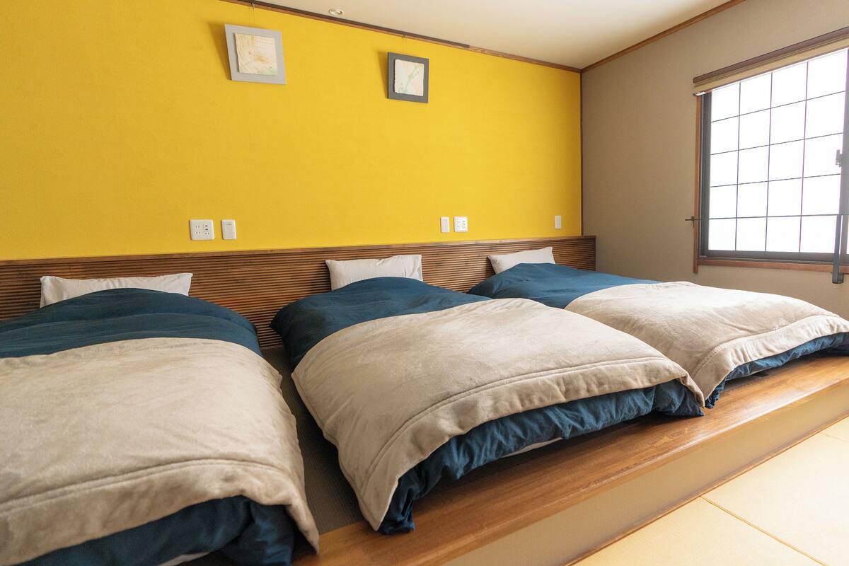 A hotel room with two beds, a window, and a yellow wall.