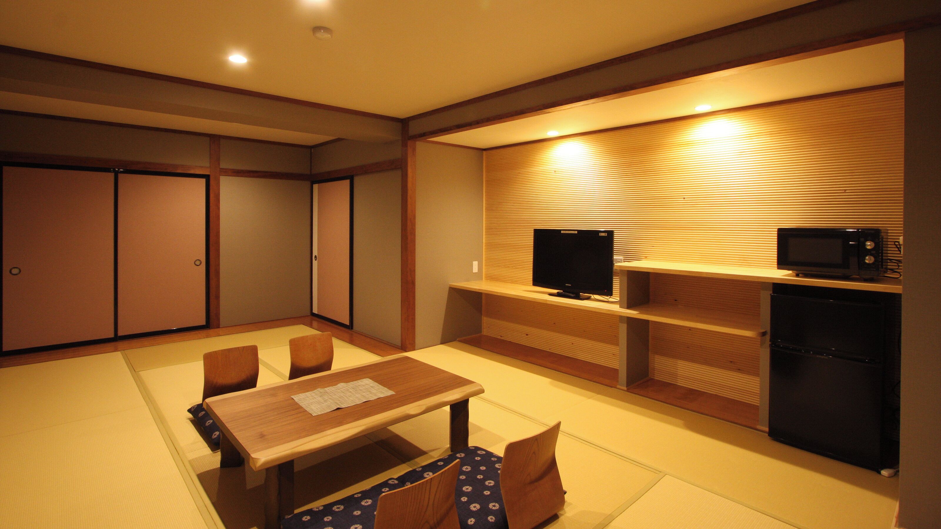 Una habitación con una mesa de comedor de madera, sillas, televisor, microondas y refrigerador.