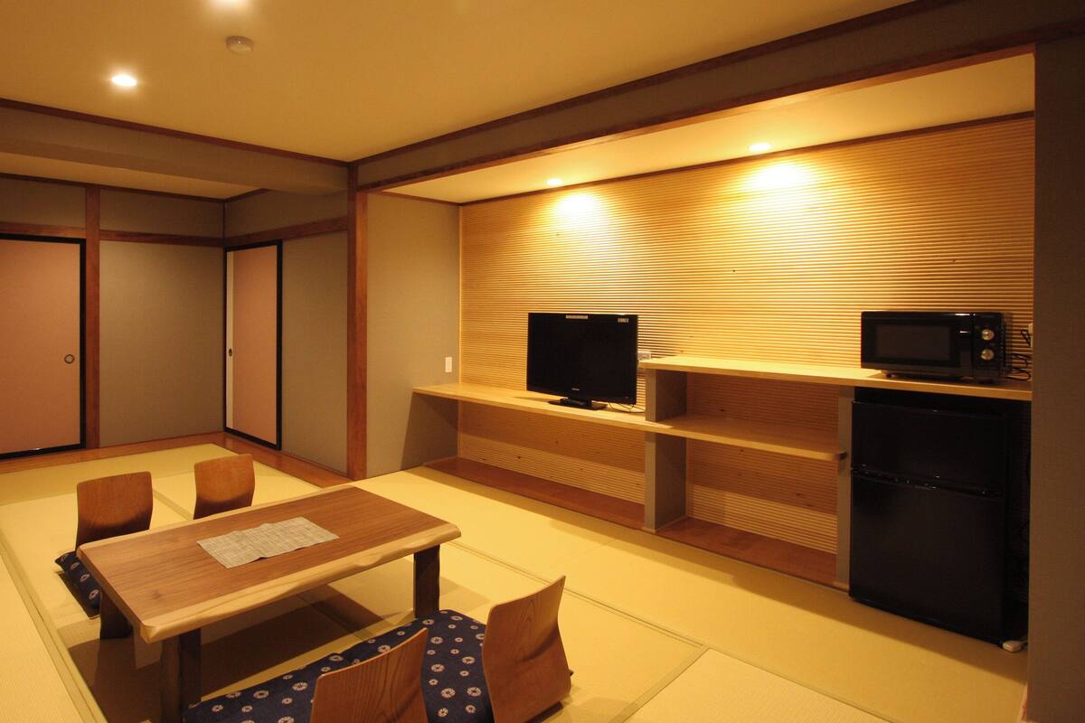A room with a wooden dining table, chairs, a television, a microwave, and a refrigerator.