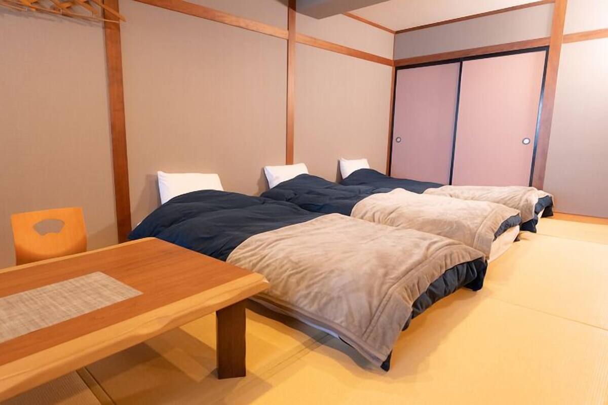 A room with two beds, a wooden table, and a wardrobe.