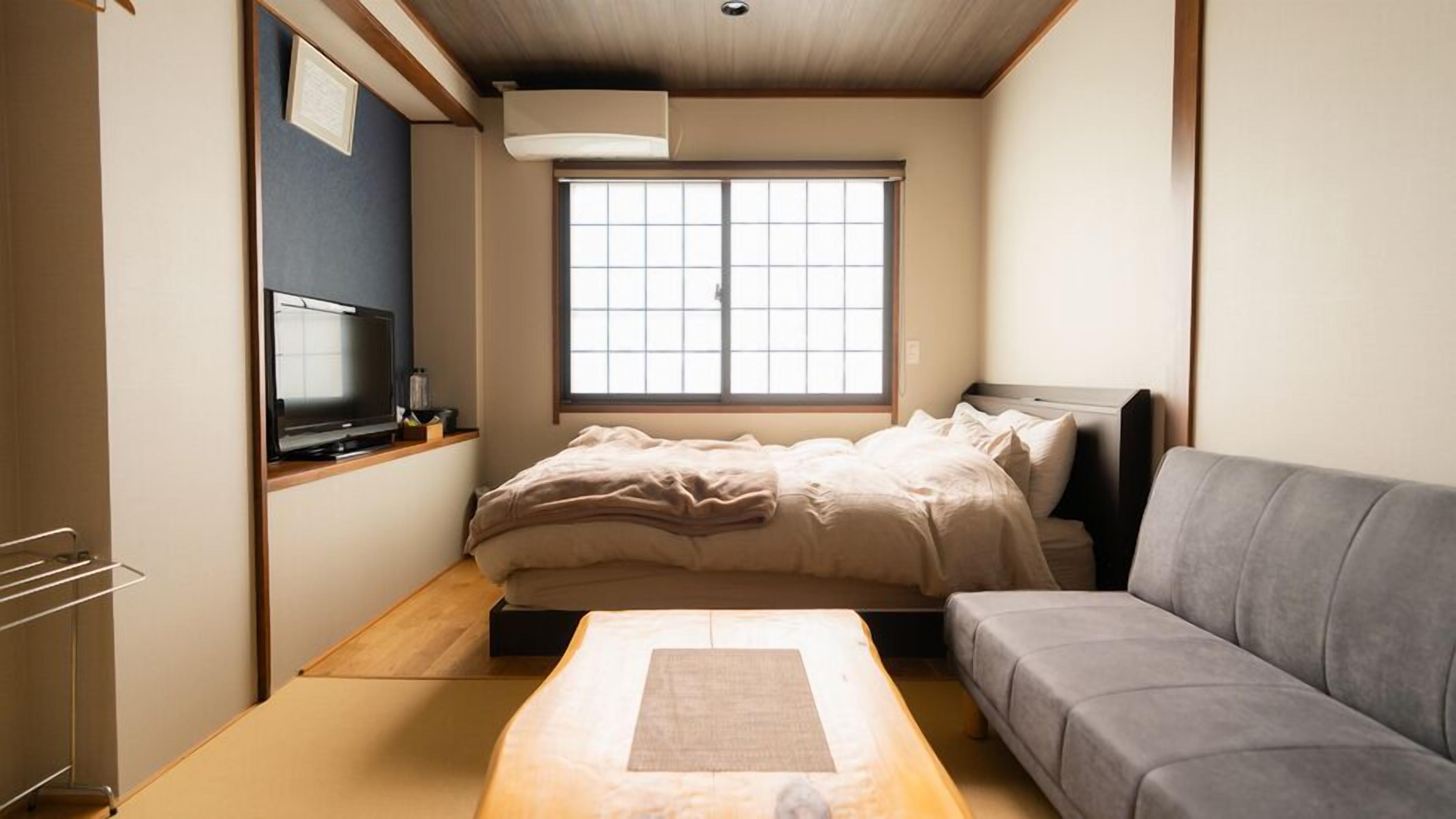 Una habitación compacta con cama, sofá gris, televisor y ventana.