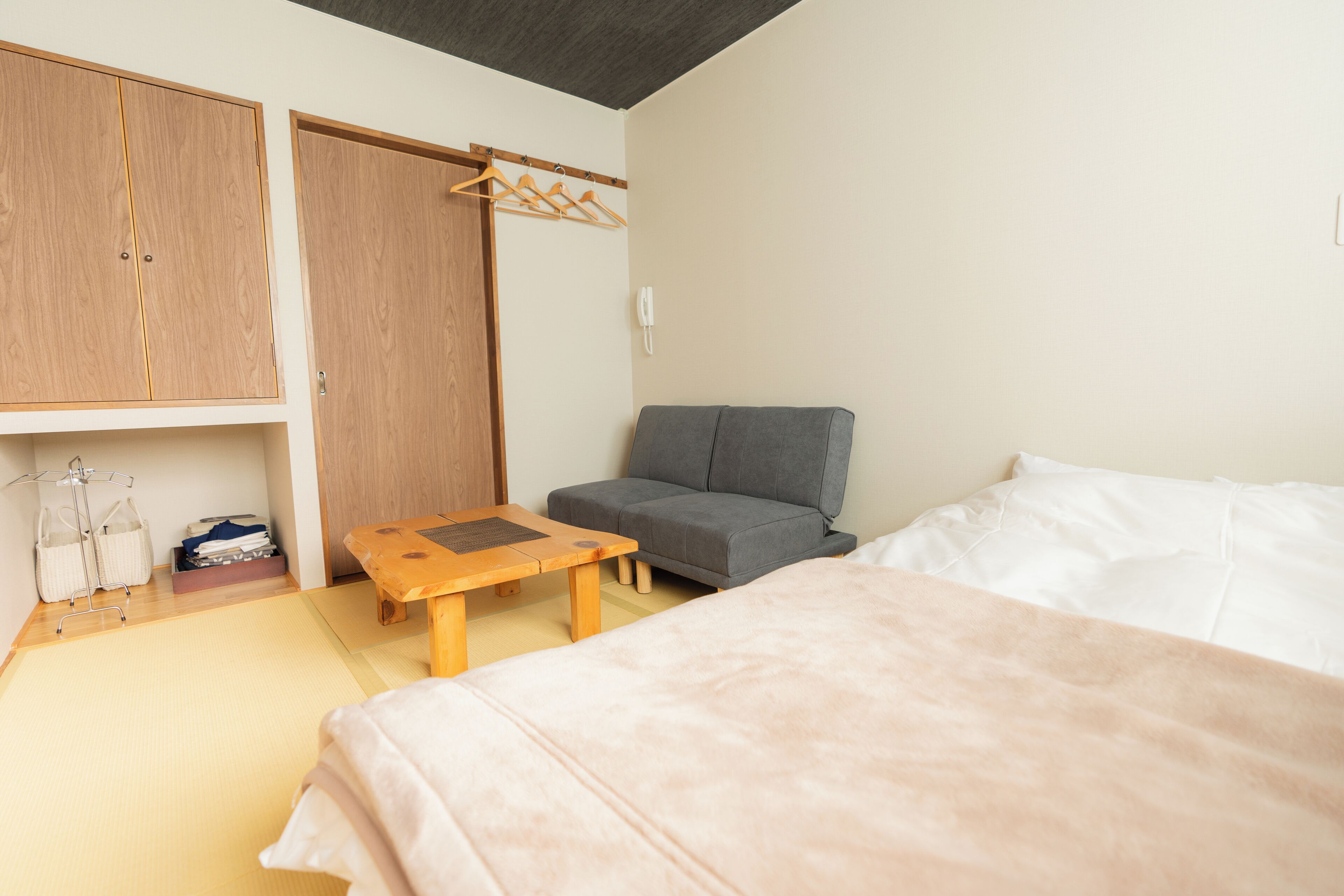 A room with a bed, a sofa, a wooden table, a wardrobe, and a telephone.