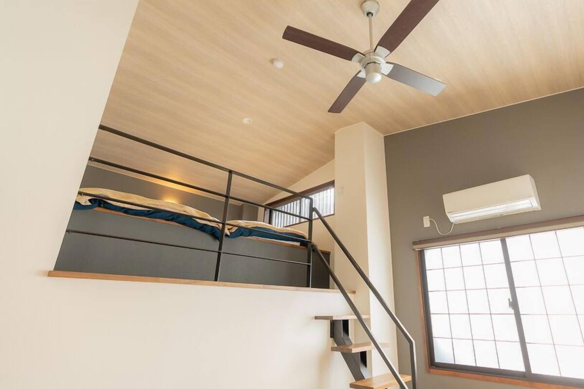 A room with a ceiling fan, a window with blinds, a staircase, and an air conditioning unit.