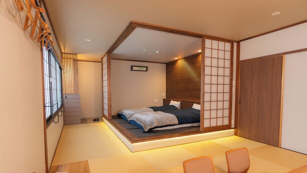 Habitació japonesa tradicional amb tatami, un llit baix sobre plataforma, portes corre diapositives shoji i un escriptori de fusta amb cadires.