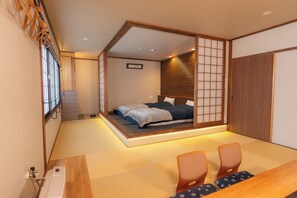 A traditional Japanese-style room with tatami flooring, a low platform bed, sliding shoji doors, and a wooden desk with chairs. - Nozawaonsen Azegamikan (Nozawaonsen)