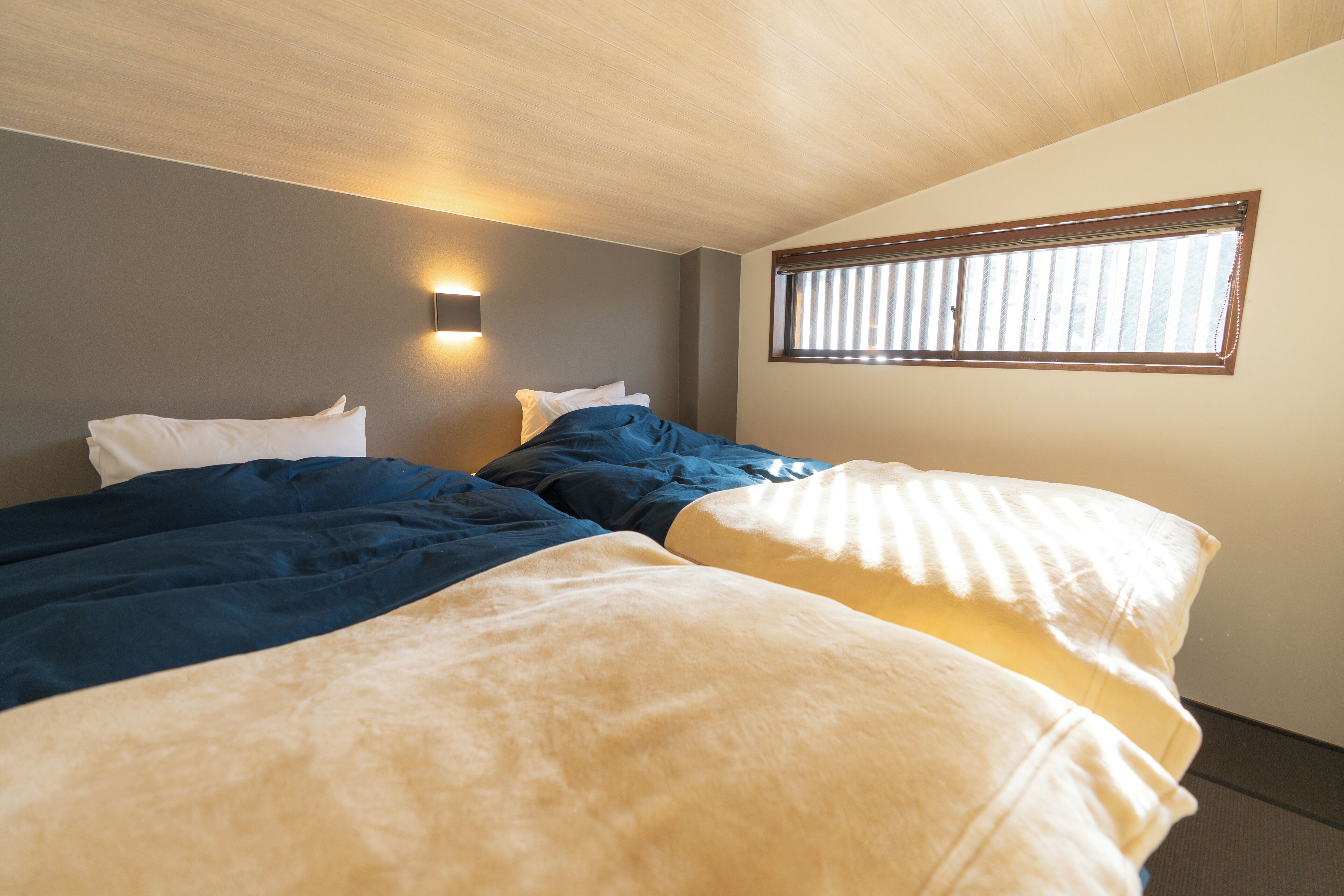A room with two beds, a window, and a wall-mounted light.