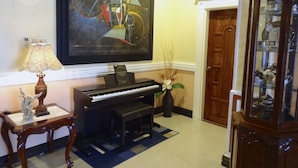A lobby with a piano, a framed abstract painting, a lamp, and a cabinet with glass doors. - The Executive Villa Inn & Suites (Davao)