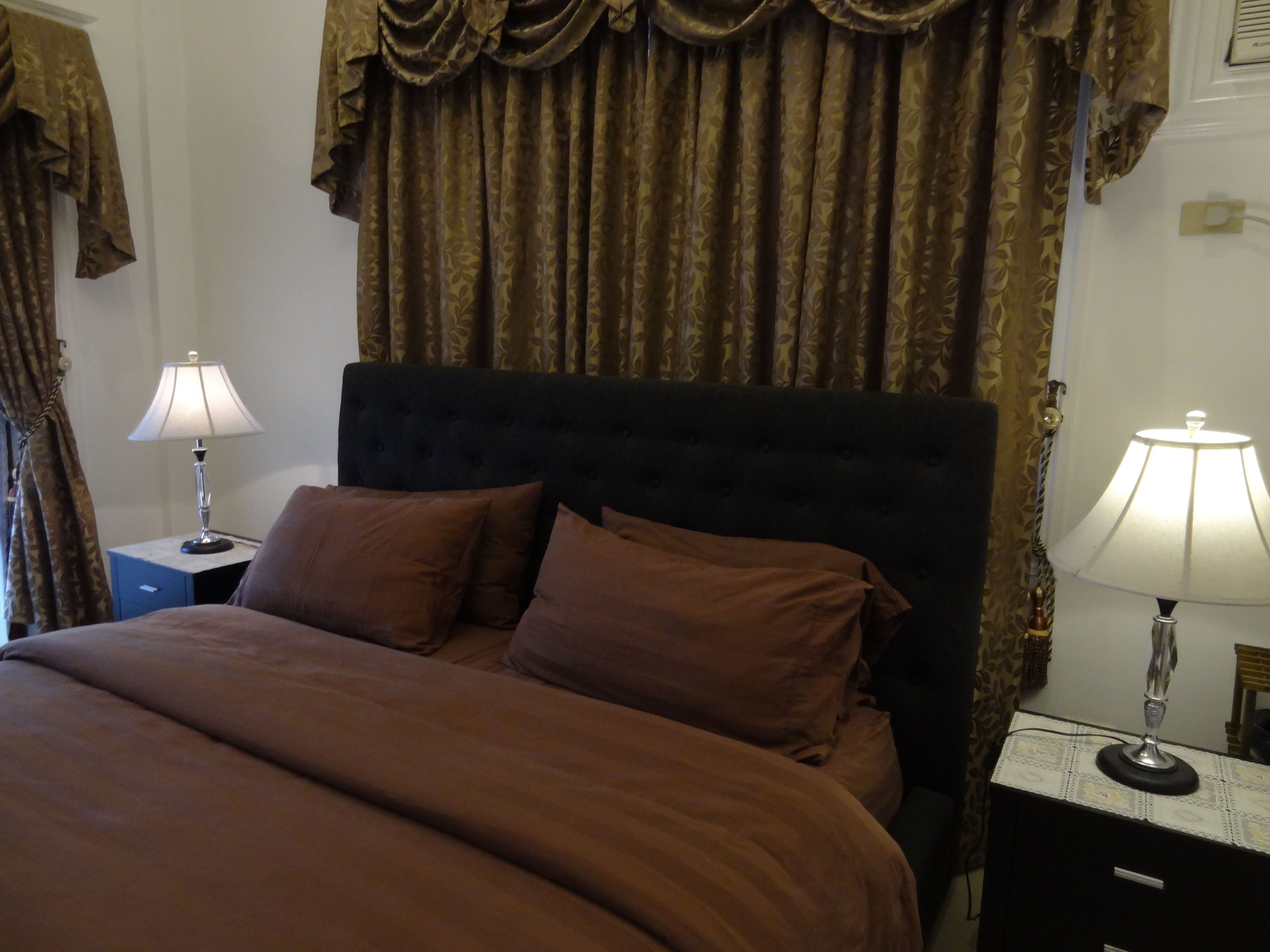 A neatly made bed with brown bedding, two bedside tables with lamps, and a dark headboard.