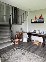 A staircase with a wooden finish, a small table with a pitcher, a wooden crate, and a rug on the floor.