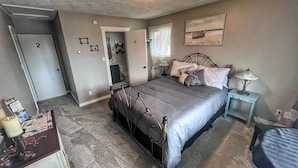 Quarto com cama, mesa de cabeceira, abajur e porta para o banheiro.