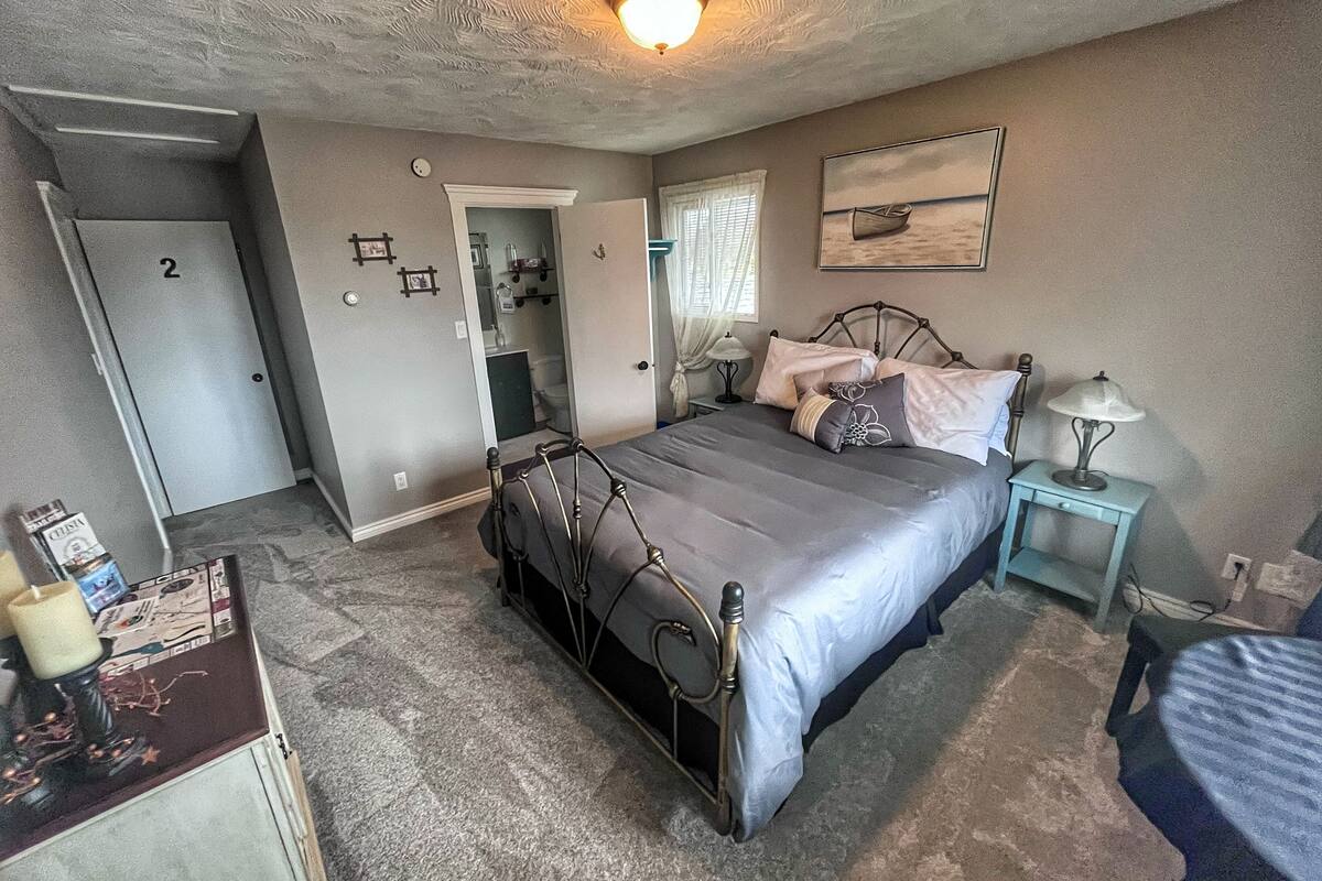 Un dormitorio con cama, mesita de noche, lámpara y puerta que da a un baño.