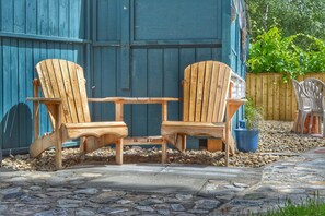 Two wooden Adirondack chairs with a small table in between, set on a stone patio with a wooden fence in the background. - Sunny Shuswap B&B (Chase)