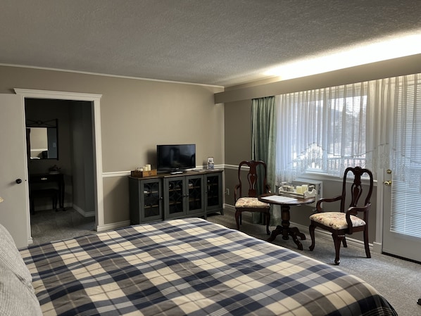 A hotel room with a large bed, a TV on a cabinet, a dining table with chairs, and a view of the outside through the window. - Sunny Shuswap B&B (Chase)