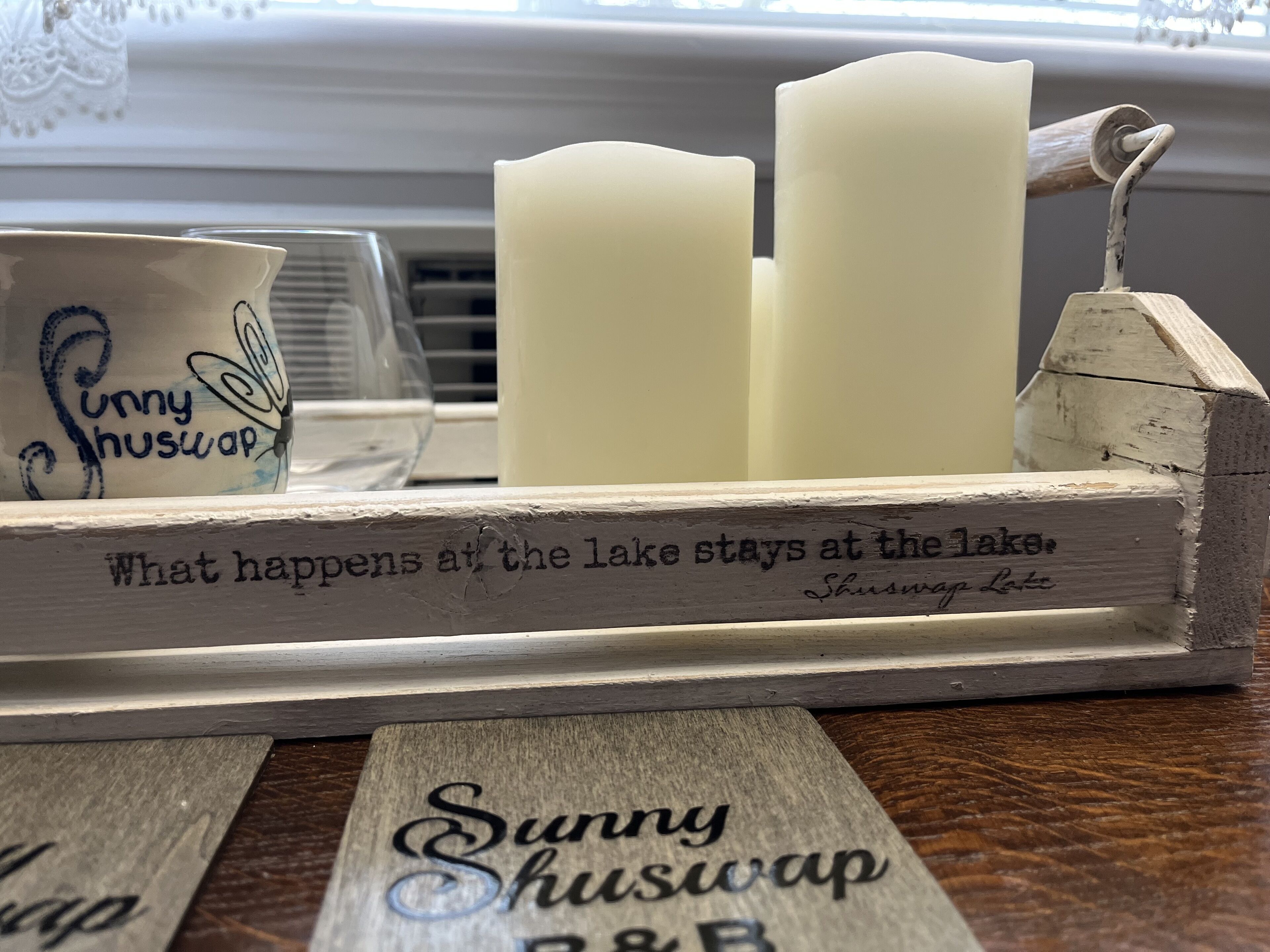 A wooden sign with the text "Sunny Shuswap B&B" and a candle holder with candles.