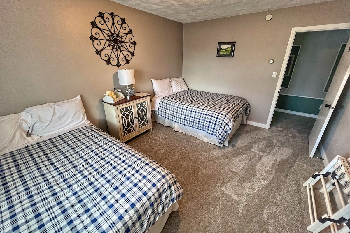 Un dormitorio con dos camas, una mesita de noche, un adorno en la pared y una puerta que da a otra habitación.