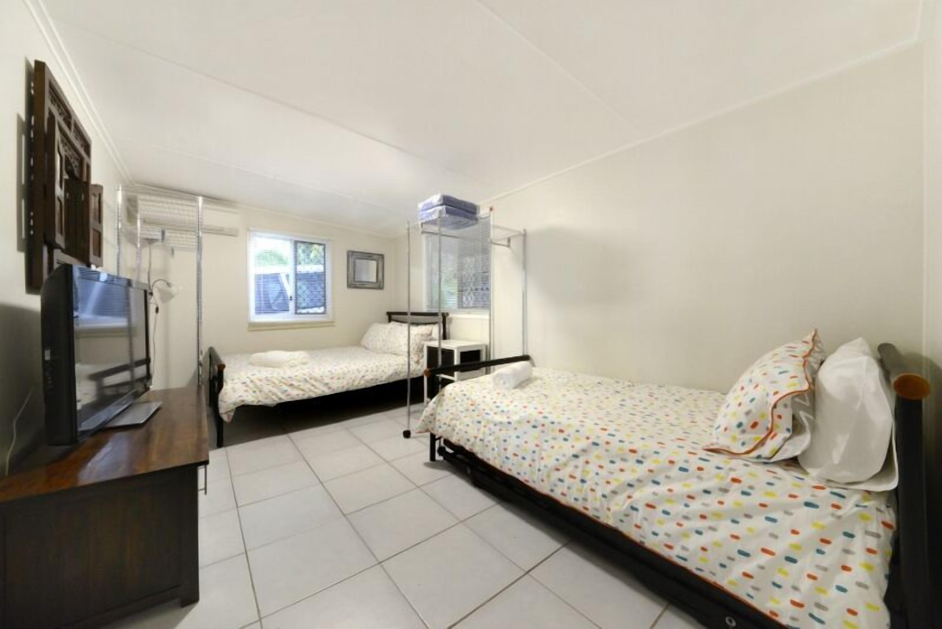 A bedroom with two beds, a desk, a TV, and a window.
