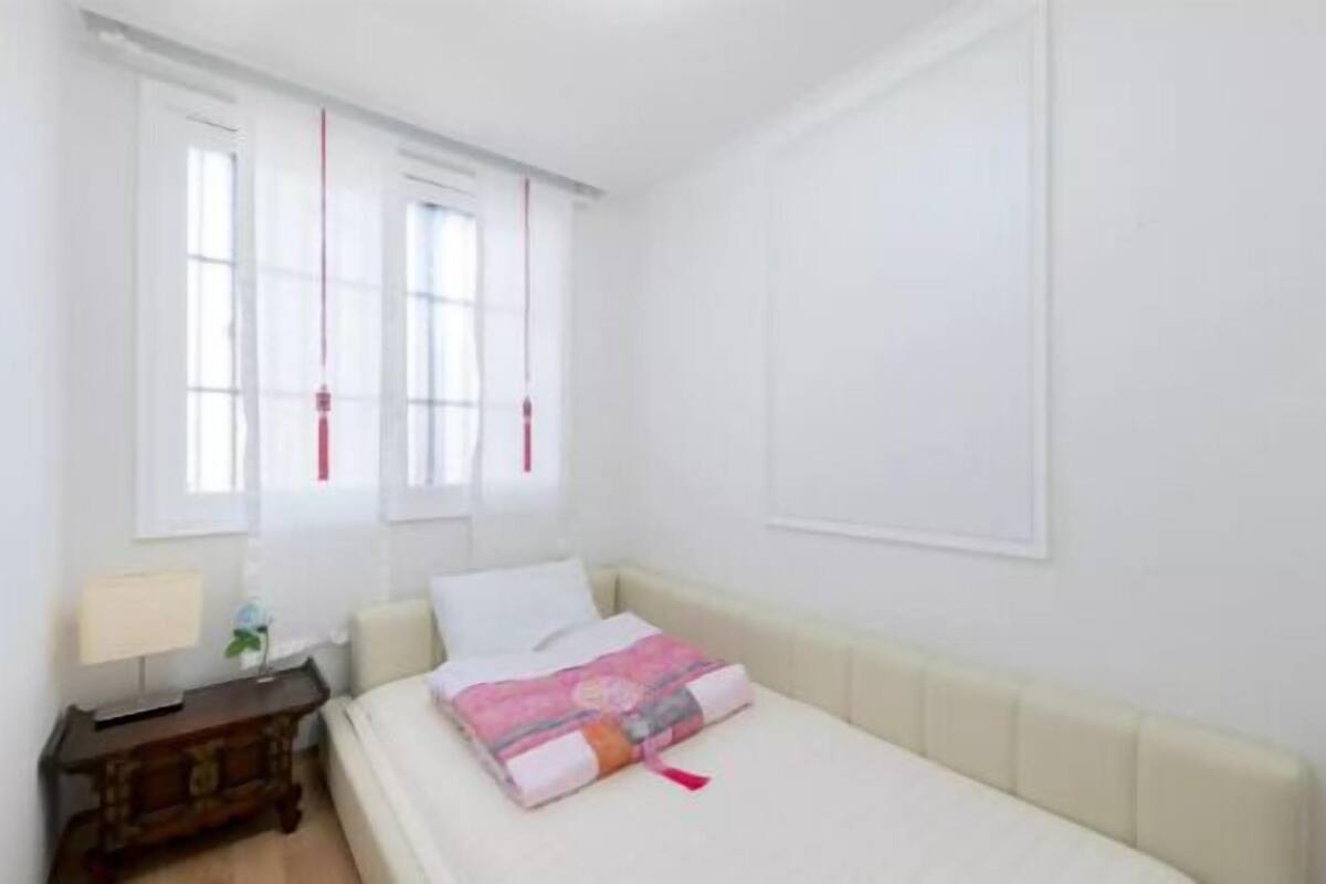 Ein Schlafzimmer mit Bett, Nachttisch, Lampe und einem Fenster mit Vorhängen.