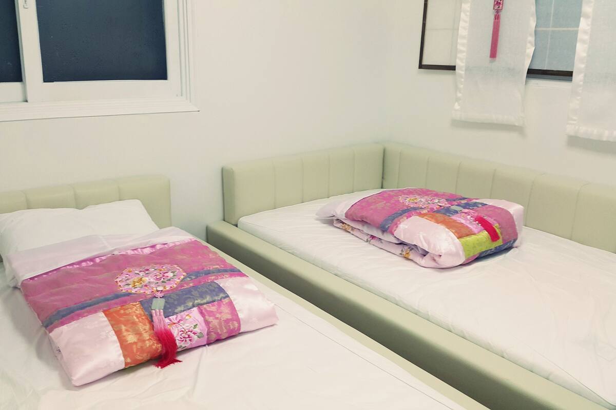 Ein Doppelbett mit einer rosa-orangenen Tagesdecke, einem weißen Kopfkissen und einem grünen Kopfteil.