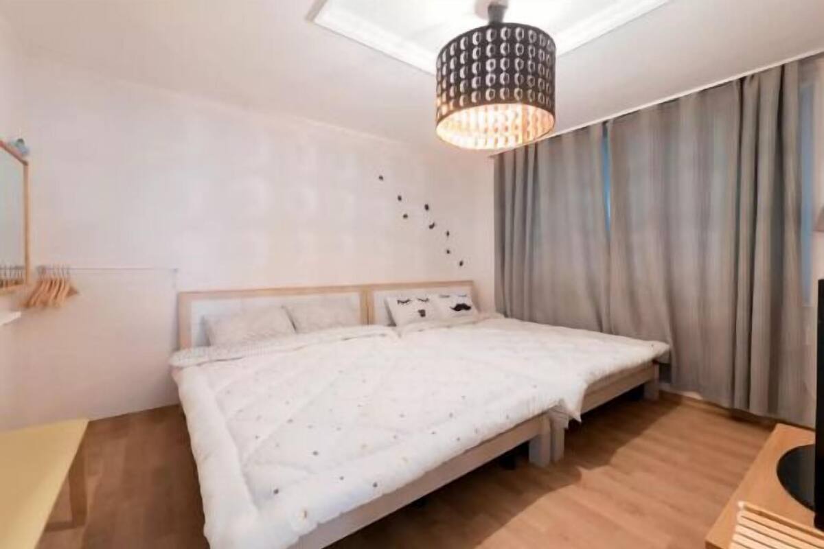 Ein Schlafzimmer mit Bett, Nachttisch, Pendelleuchte und einem fenster mit Vorhängen.